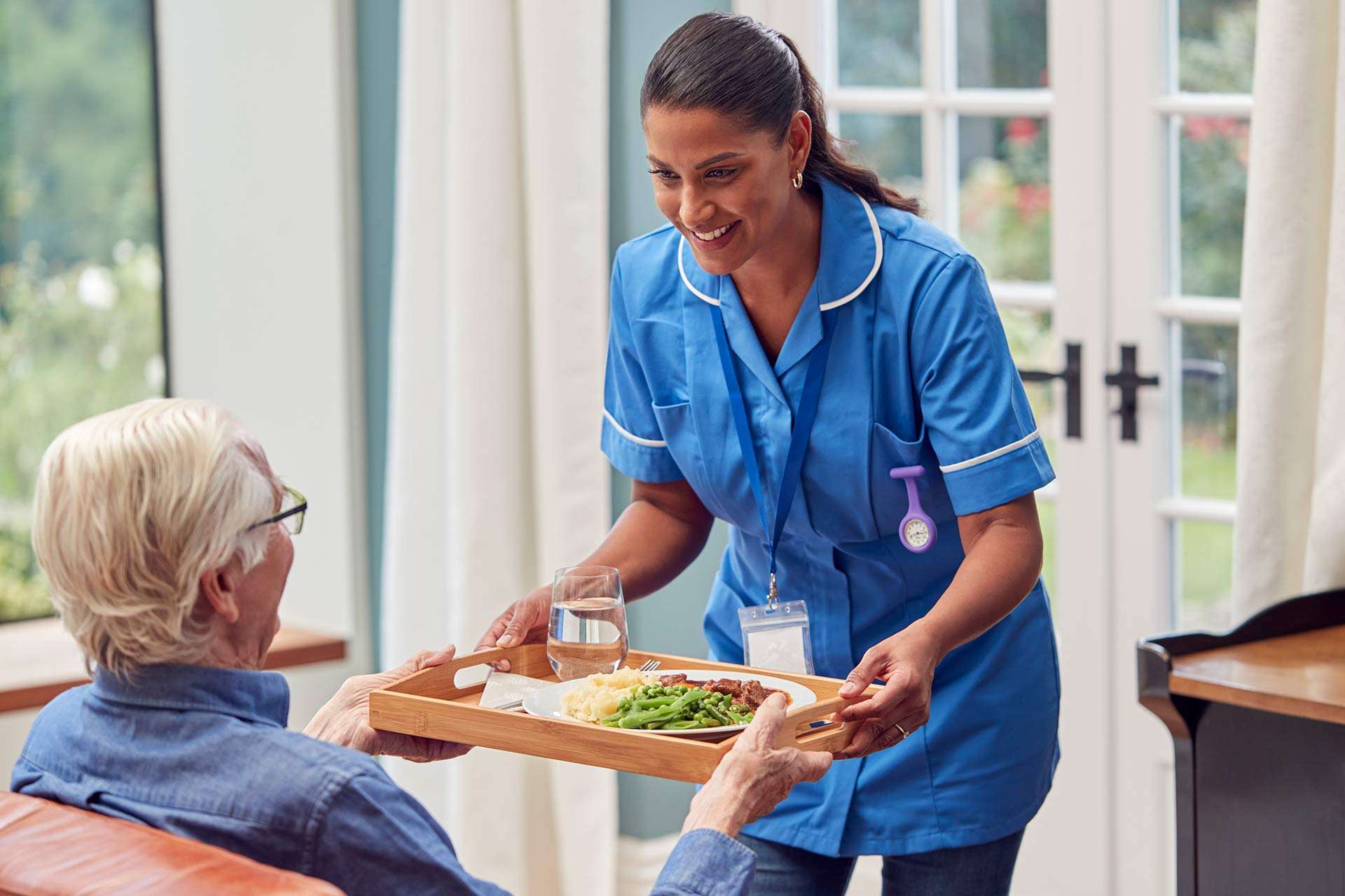 female care worker in uniform bringing meal on tray